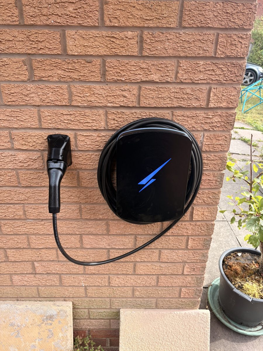 Black home EV charger with tethered cable mounted on a red brick wall